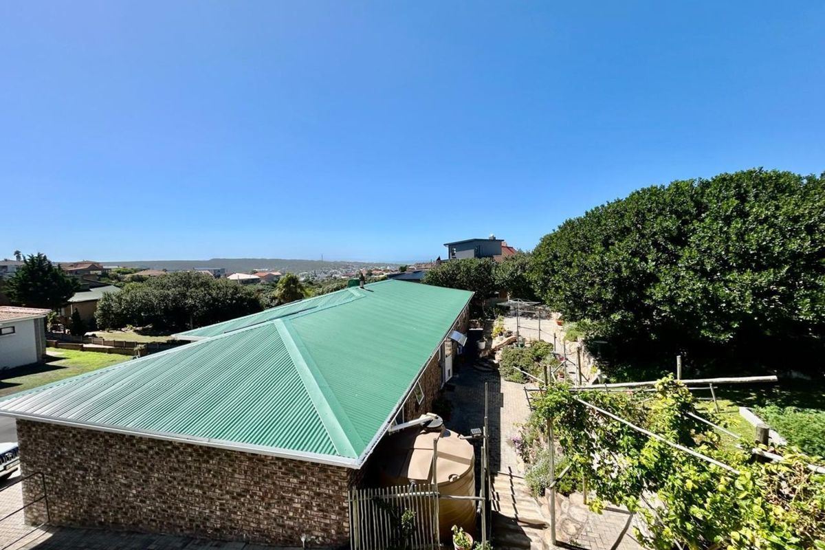 Elevated view of the property featuring a green corrugated metal roof, brick exterior walls, a water storage tank, and a landscaped garden area.