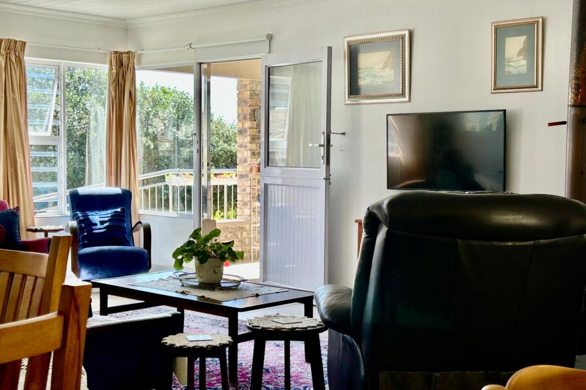 A bright living room featuring large windows and a glass door providing direct access to an outdoor patio area.