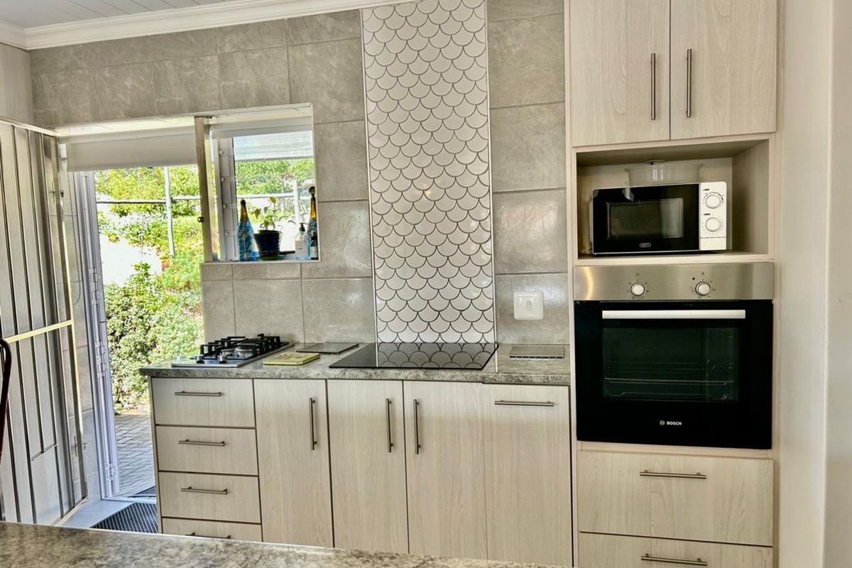 Modern kitchen featuring light wood cabinetry, granite countertops, a built-in oven, and a decorative scalloped tile backsplash with direct access to the garden.