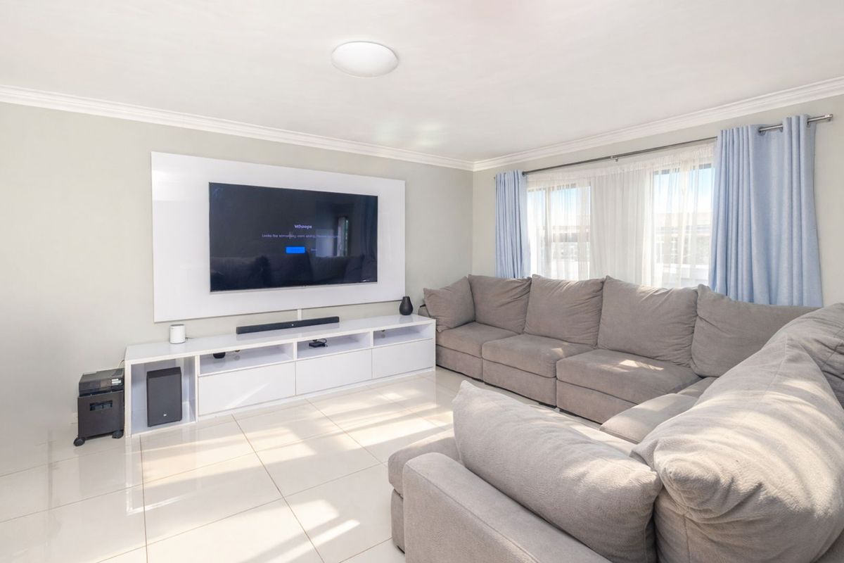 A bright and modern living room featuring tiled flooring, crown molding, and a built-in media wall unit.