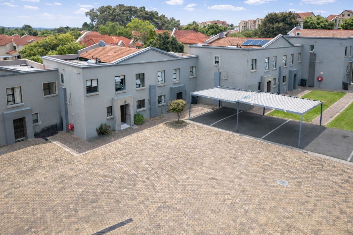 Aerial view of the property complex featuring paved courtyard, covered parking bays, and multi-story residential building with tiled roofing.