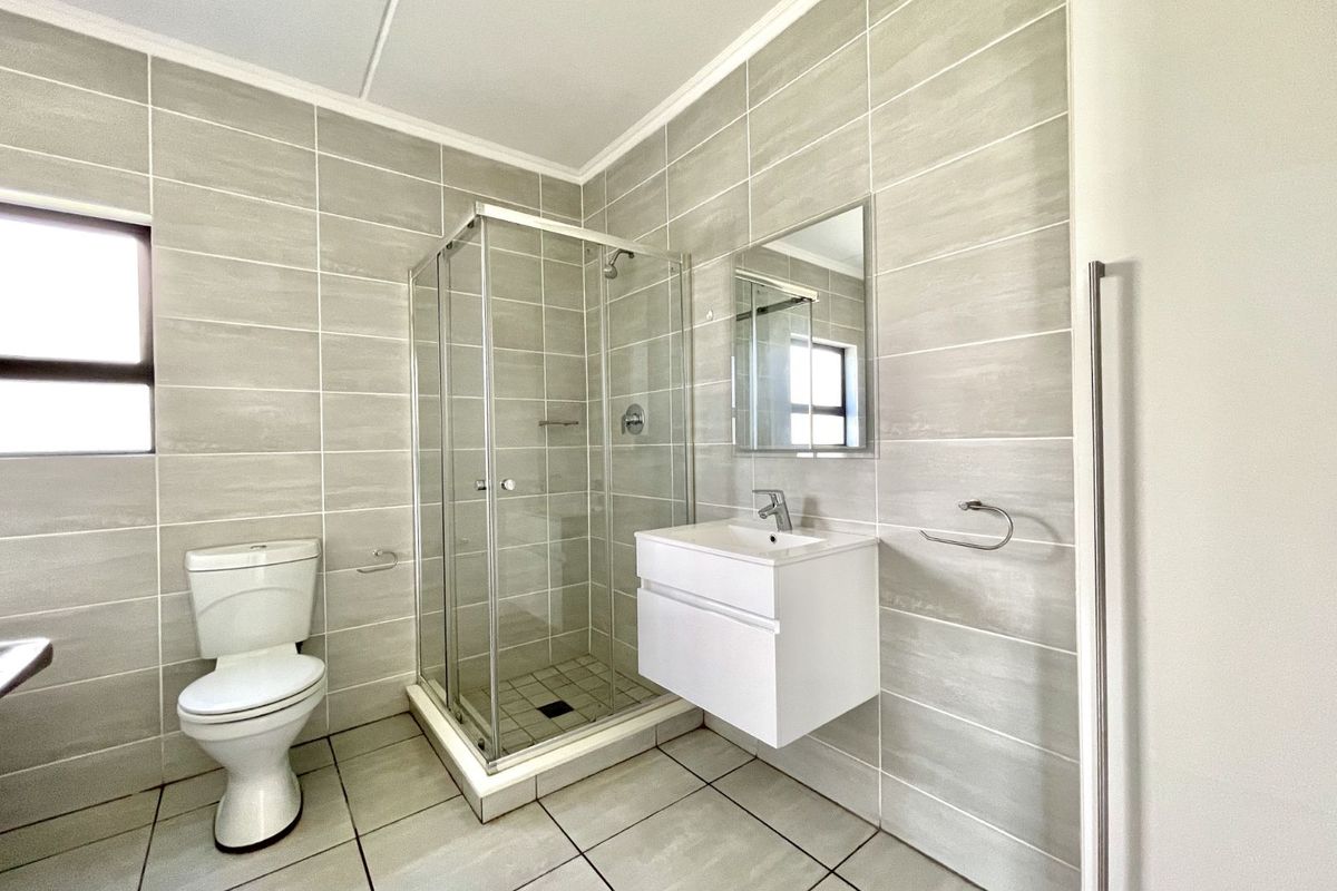 A modern bathroom featuring floor-to-ceiling neutral tiling, a glass-enclosed shower, a wall-mounted vanity with a basin, and a standard toilet.