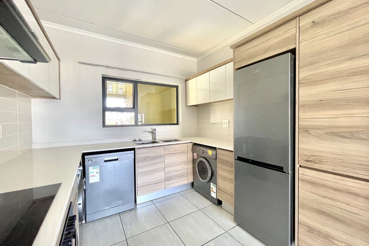 Modern kitchen featuring light wood-grain cabinetry, stone countertops, integrated sink, and built-in appliance spaces with tiled flooring.