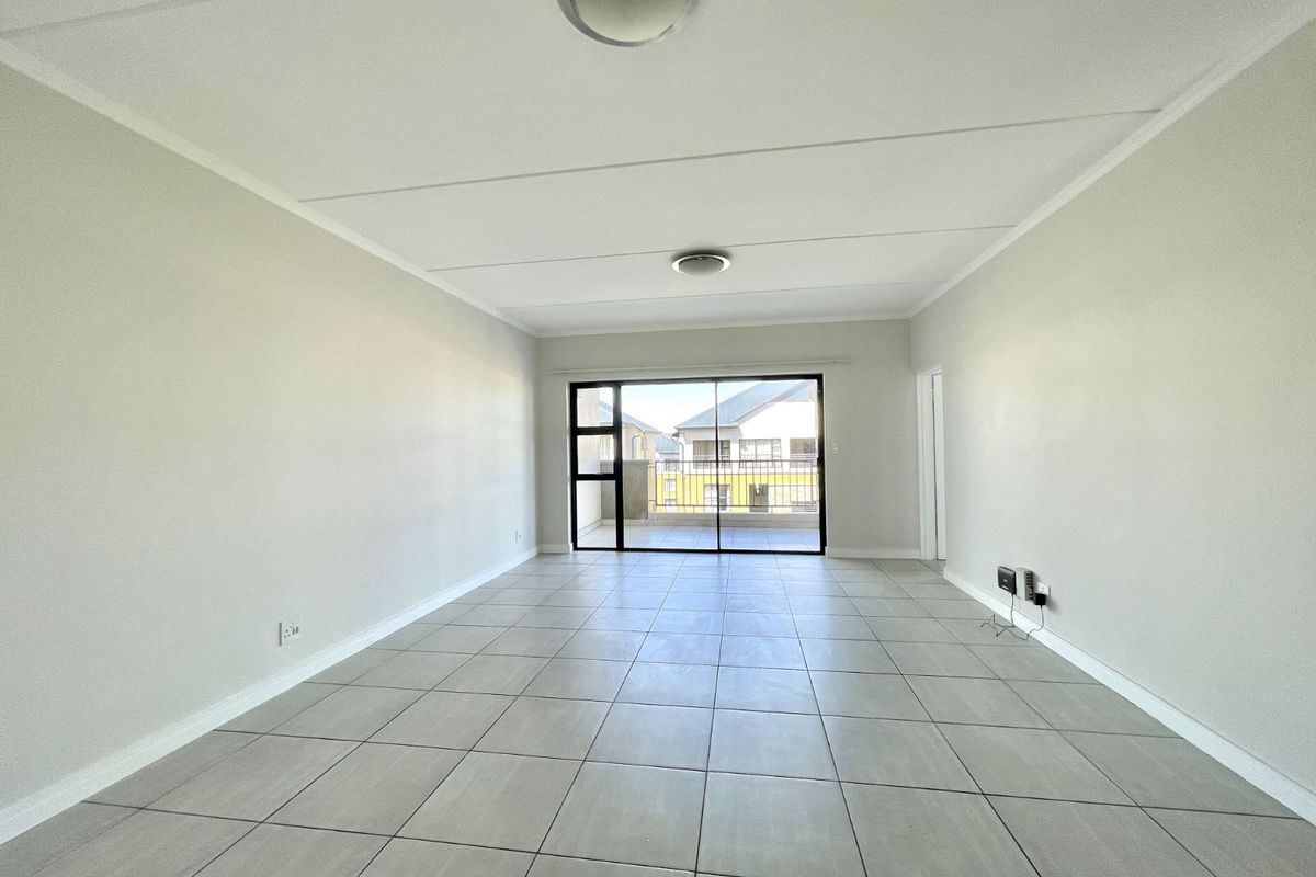 A bright, open-plan living area featuring neutral tiled flooring, clean walls, and large sliding glass doors leading to an outdoor balcony.