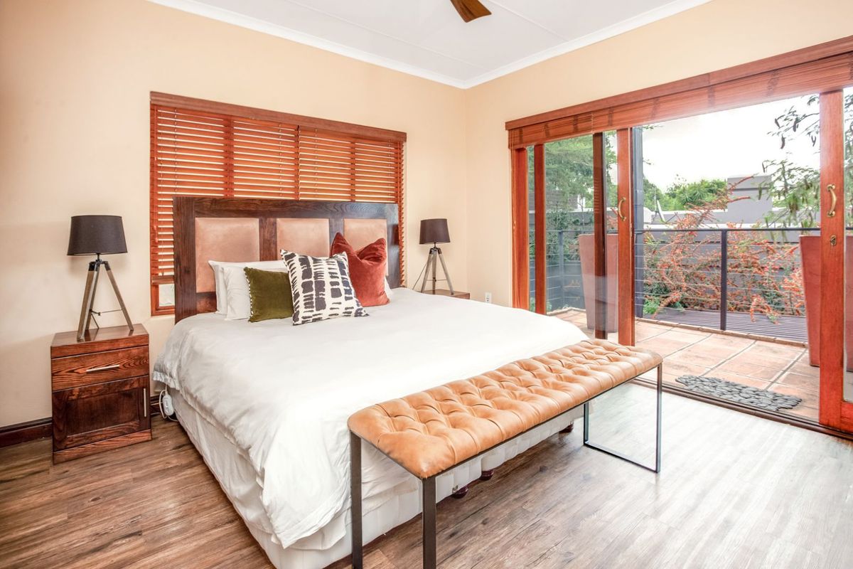 A well-maintained bedroom featuring wood-look flooring, timber window blinds, and large sliding glass doors providing direct access to an outdoor balcony.