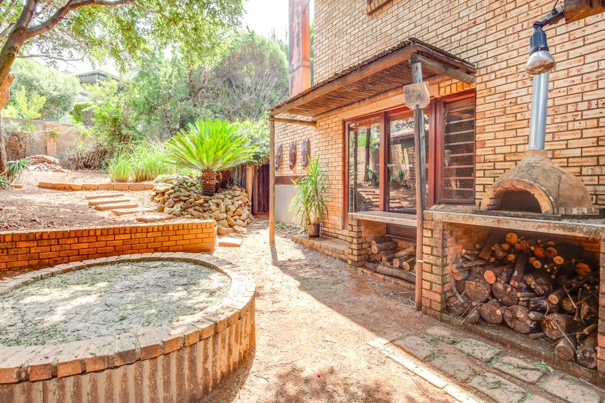 Outdoor entertainment area featuring a built-in brick pizza oven, covered patio space, and a circular brick fire pit set within a natural garden.