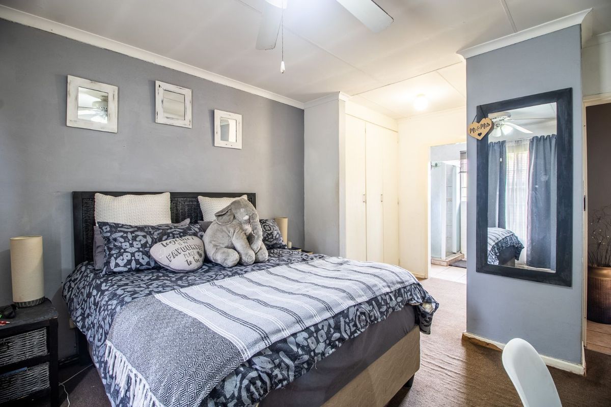A bedroom featuring built-in cupboards and an adjoining en-suite bathroom, finished with neutral wall tones and carpeted flooring.