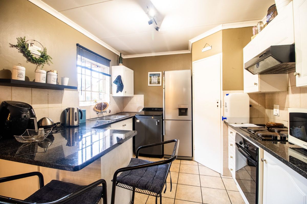 A functional kitchen featuring granite countertops, built-in oven, extractor fan, and tiled flooring with a breakfast nook area.