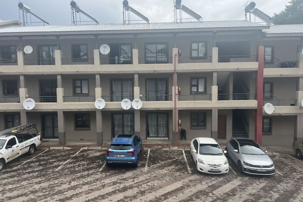 Exterior view of a multi-story apartment complex featuring balcony access, solar water heaters, and paved parking area.