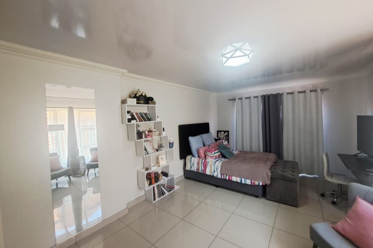Spacious bedroom featuring large format floor tiles, recessed ceiling lighting, and a neutral color palette with access to an adjoining living area.