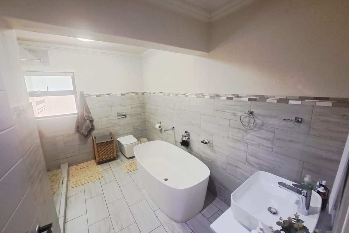 A modern bathroom featuring a freestanding bathtub, a contemporary vessel sink, and neutral wall and floor tiling.
