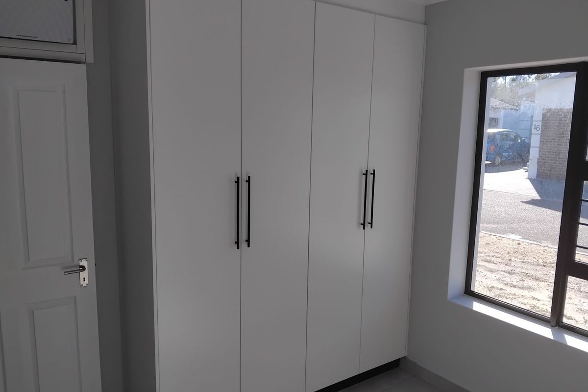 A bedroom featuring modern, floor-to-ceiling built-in wardrobes with sleek black handles and a window providing natural light.