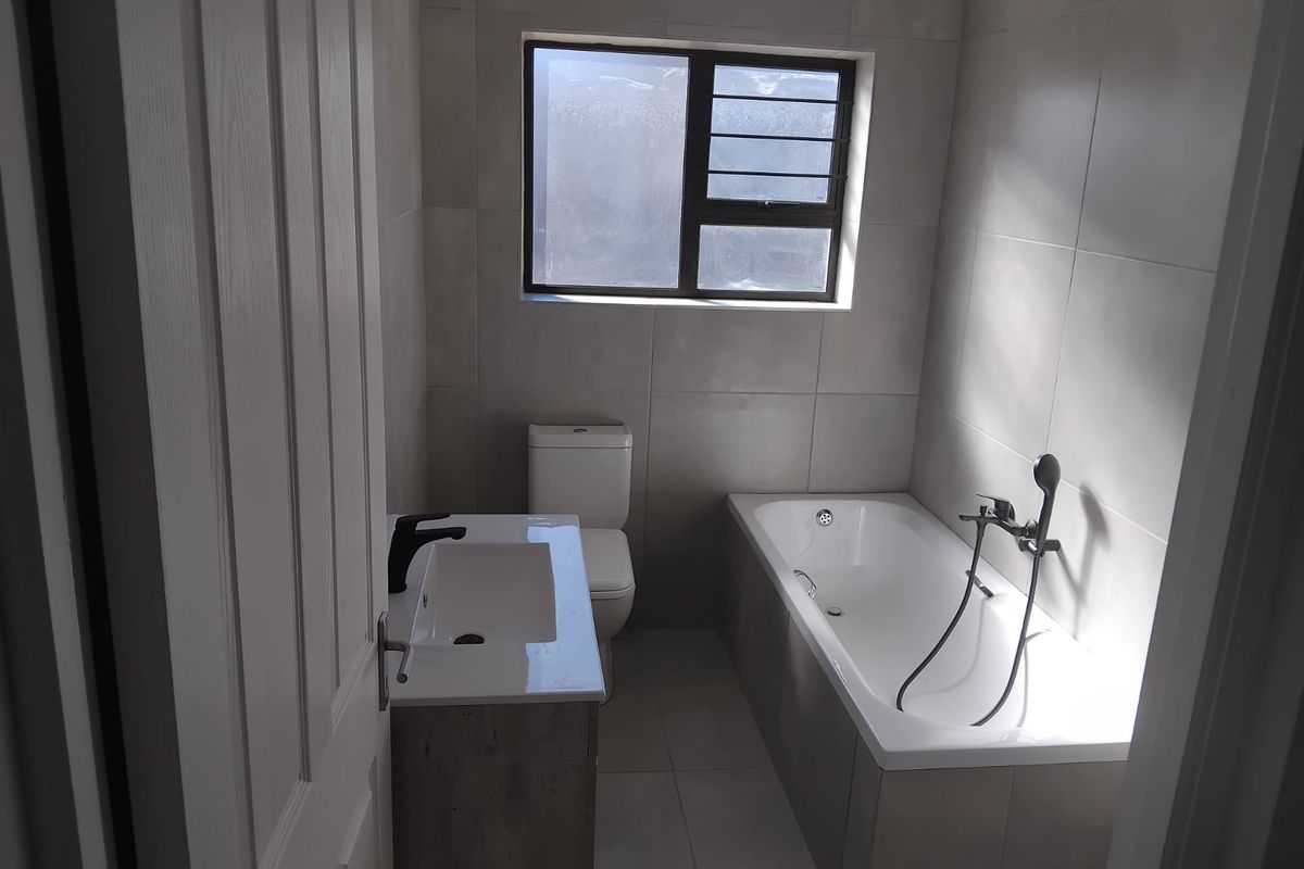 A modern bathroom featuring neutral wall tiles, a built-in bathtub with a handheld shower mixer, a vanity basin, and a toilet.