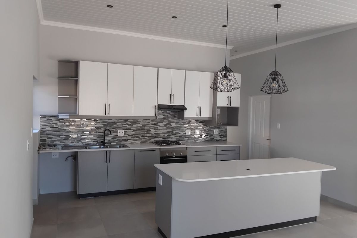 Modern kitchen featuring two-tone cabinetry, stone countertops, a central island, built-in oven, gas hob, extractor fan, and a mosaic tile backsplash.