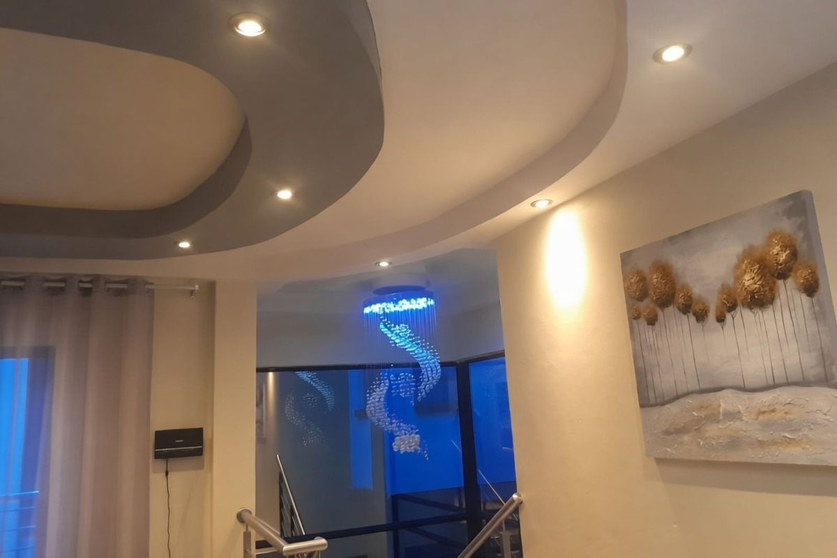 A modern living area featuring a distinctive recessed ceiling design with integrated downlighting and a contemporary spiral crystal chandelier.