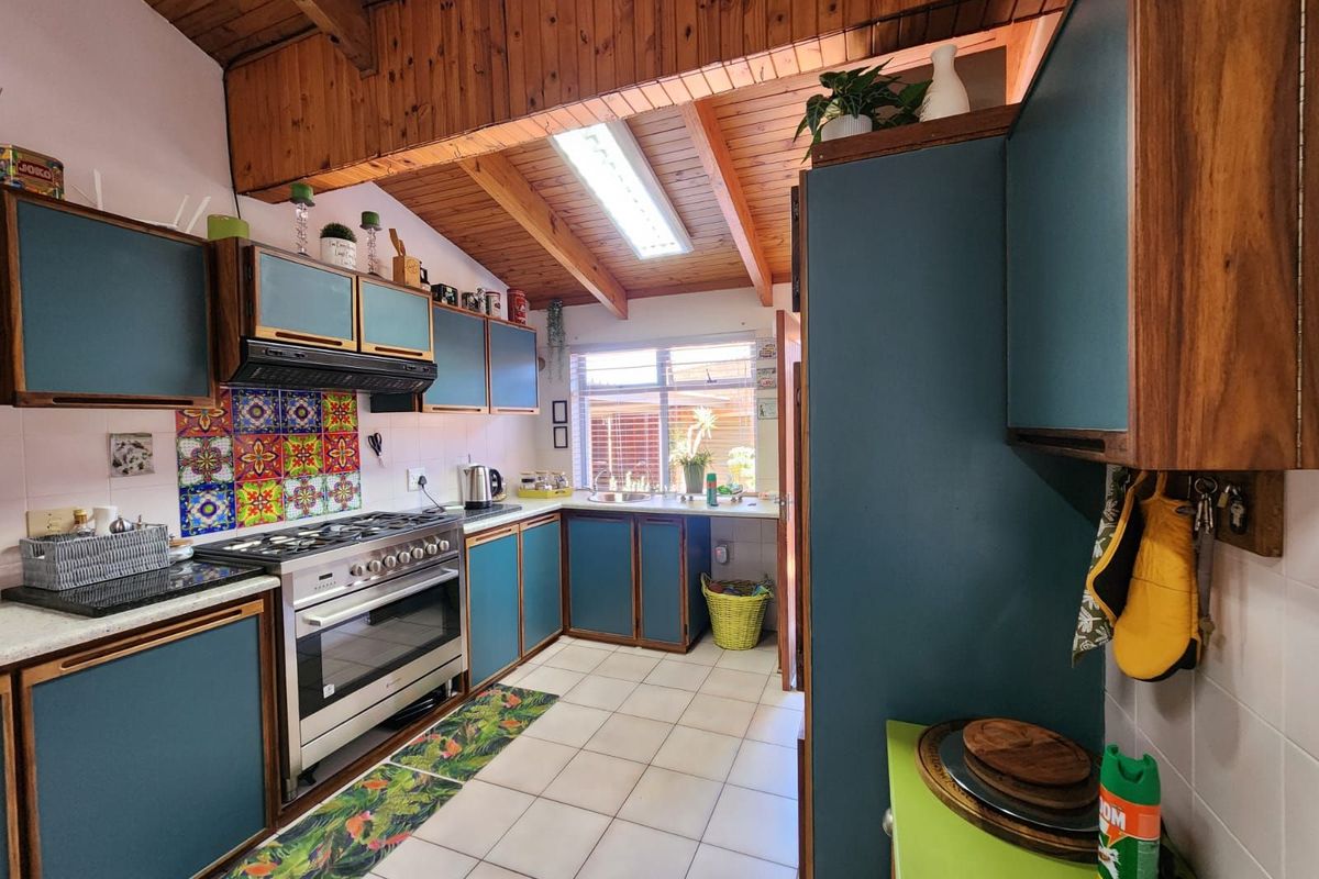 A functional kitchen featuring blue cabinetry, a gas stove with extractor fan, tiled flooring, and a vaulted timber-paneled ceiling with a skylight.