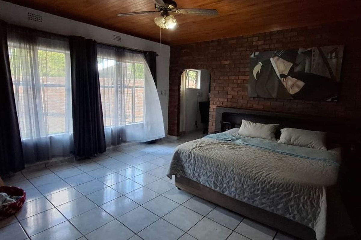Spacious bedroom featuring exposed brick feature wall, tiled flooring, and timber-clad ceiling with integrated fan.