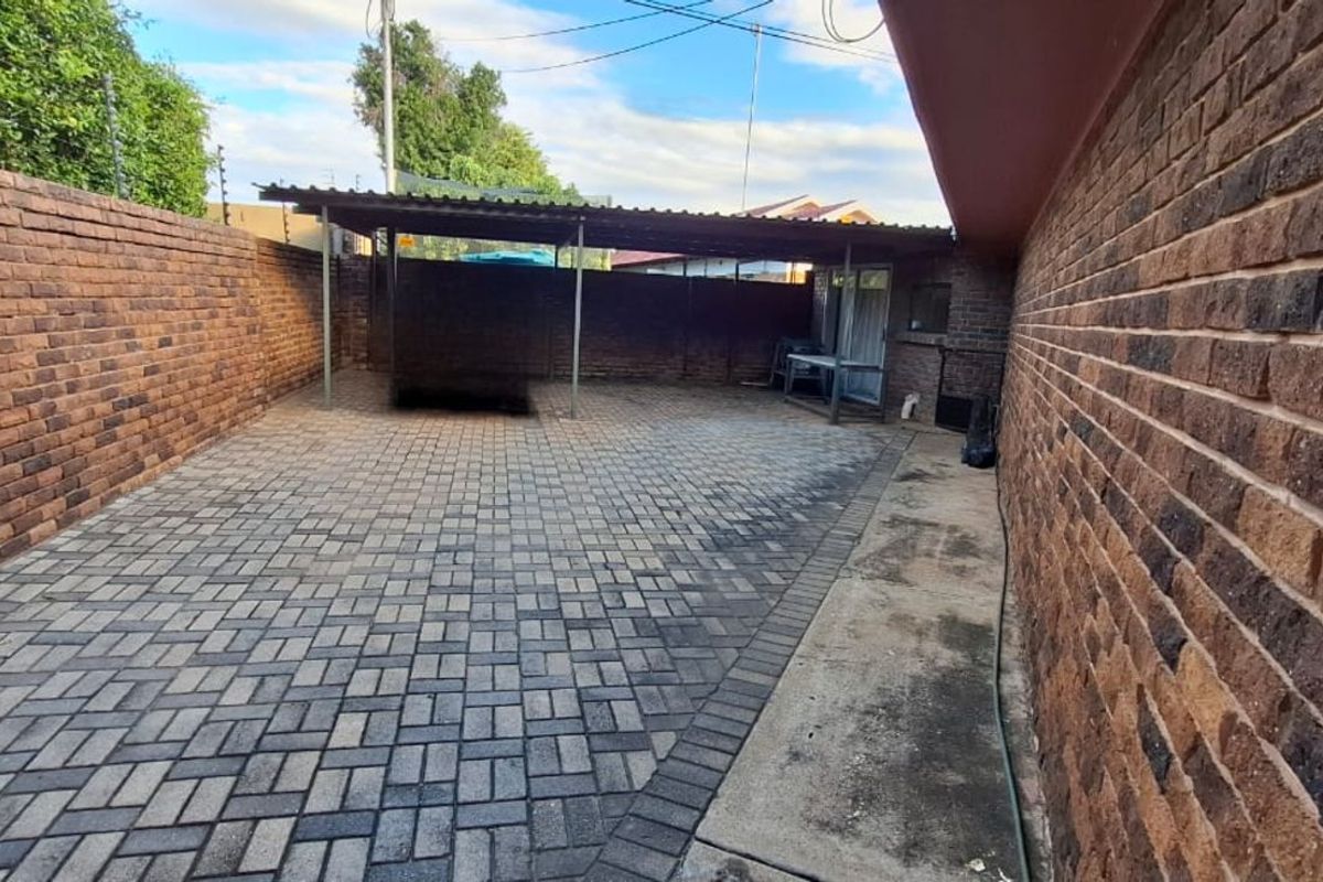 A paved rear courtyard area featuring a covered patio structure, enclosed by high face-brick boundary walls.