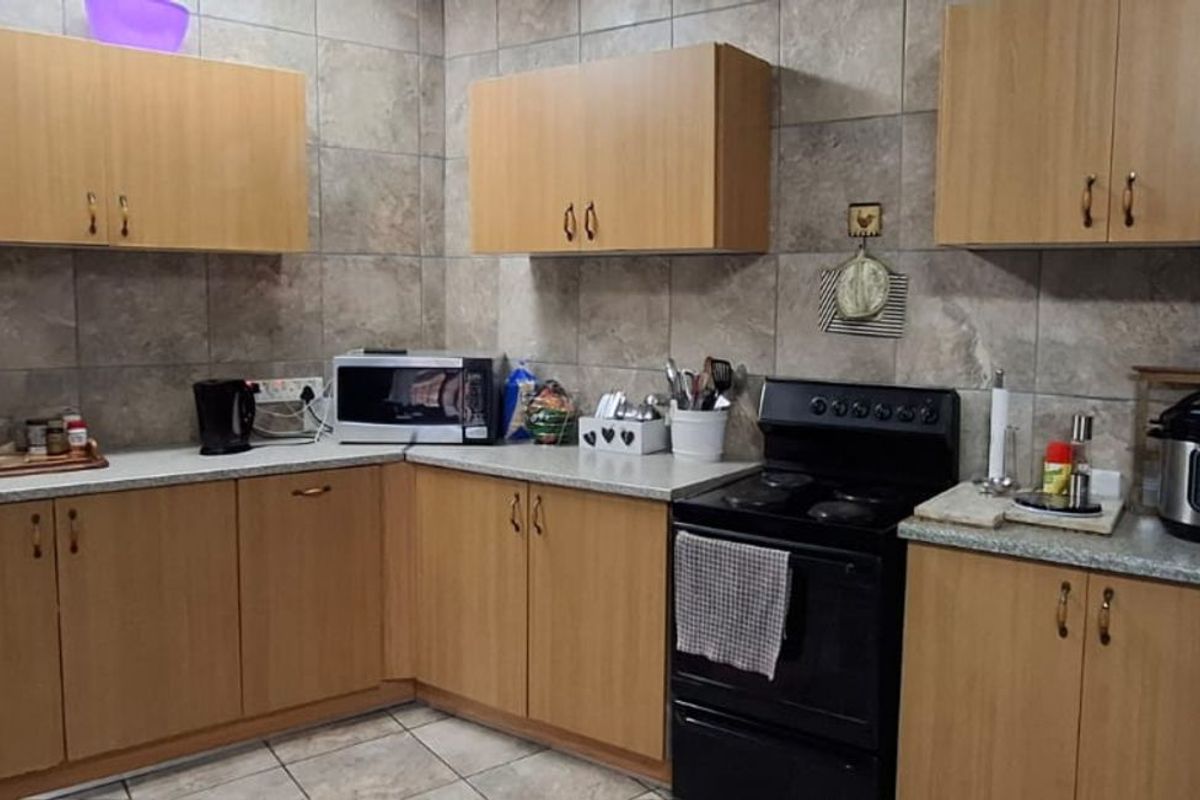A functional kitchen featuring light wood-finish cabinetry, stone-look wall tiling, and a freestanding electric stove.