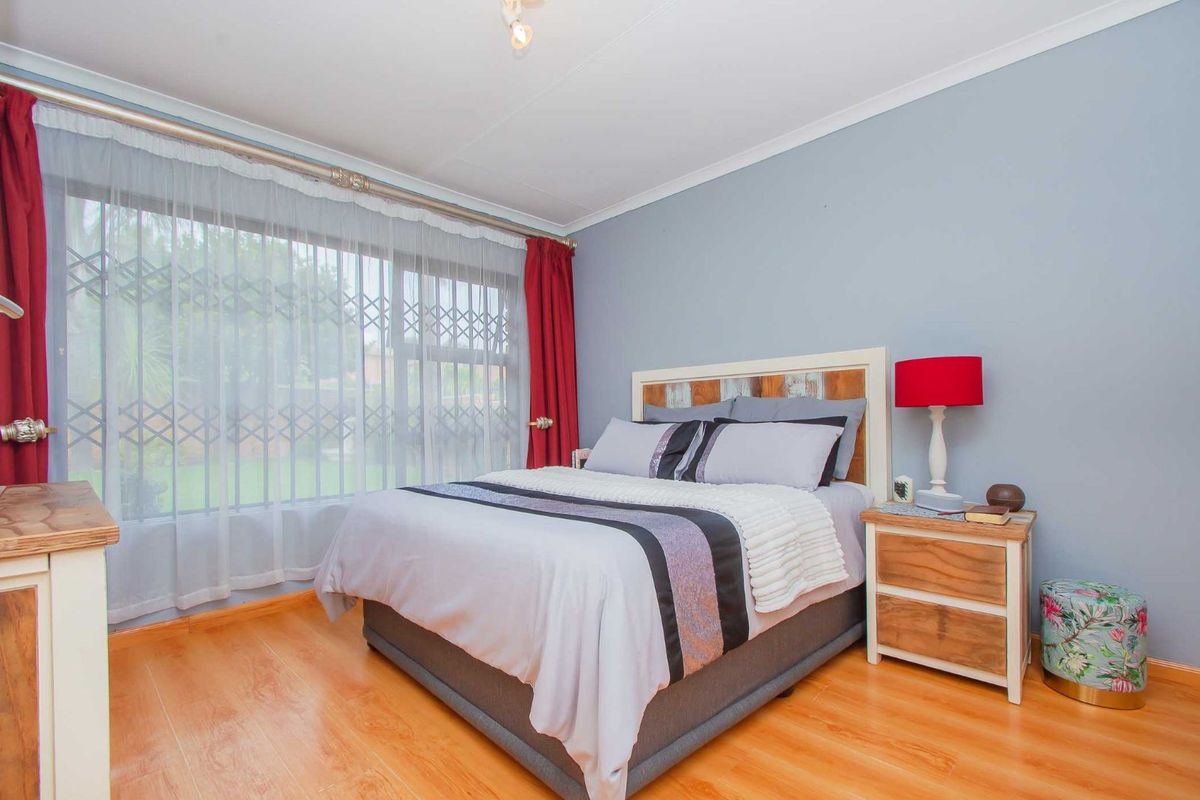A well-lit bedroom featuring laminate flooring, large windows with security bars, and neutral wall finishes, providing a comfortable and functional living space.