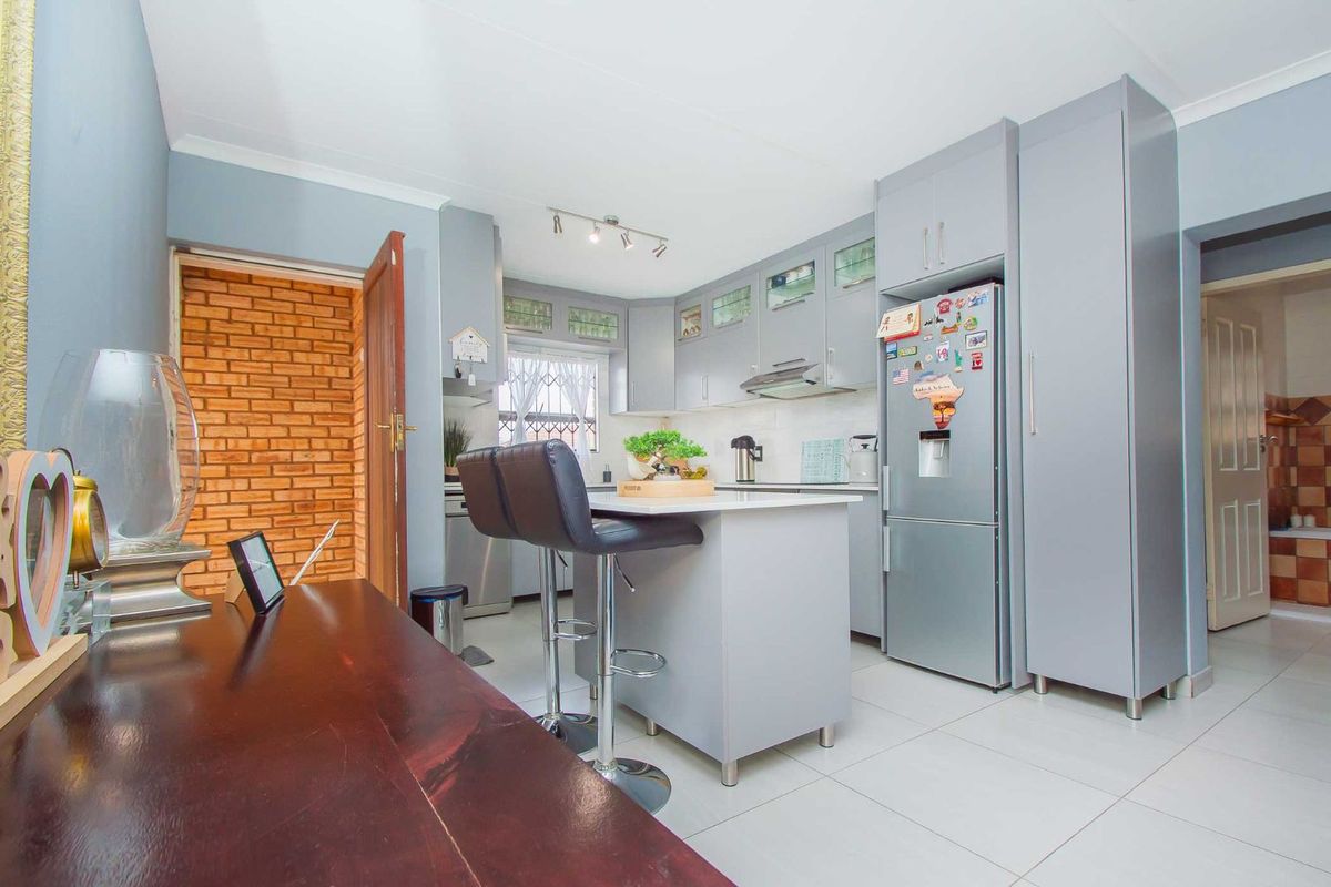 Modern kitchen featuring grey cabinetry, a central island, tiled flooring, and integrated appliances, offering a clean and functional culinary space.