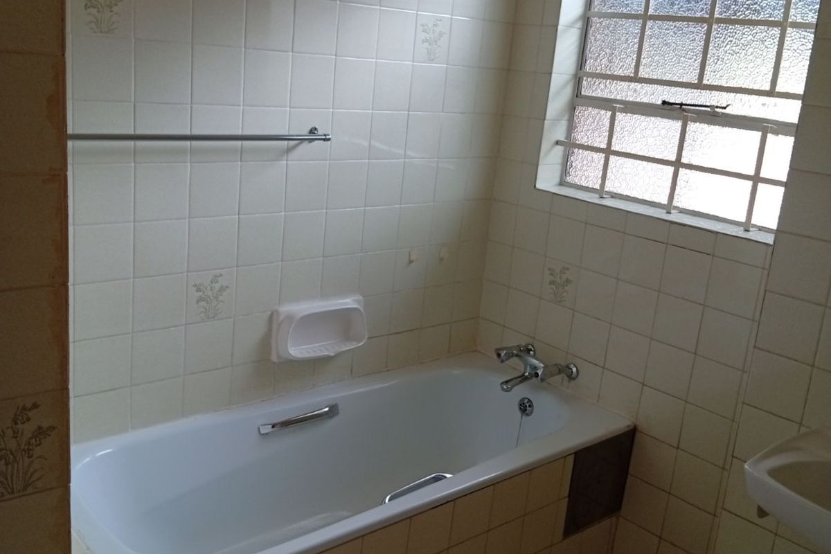 A dated bathroom featuring a built-in bathtub with tiled surround, wall-mounted soap dish, and a privacy window.