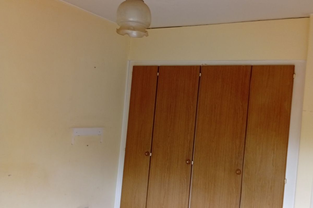 A bedroom featuring built-in wooden wardrobes, neutral wall paint, and carpeted flooring, offering a blank canvas for potential updates.