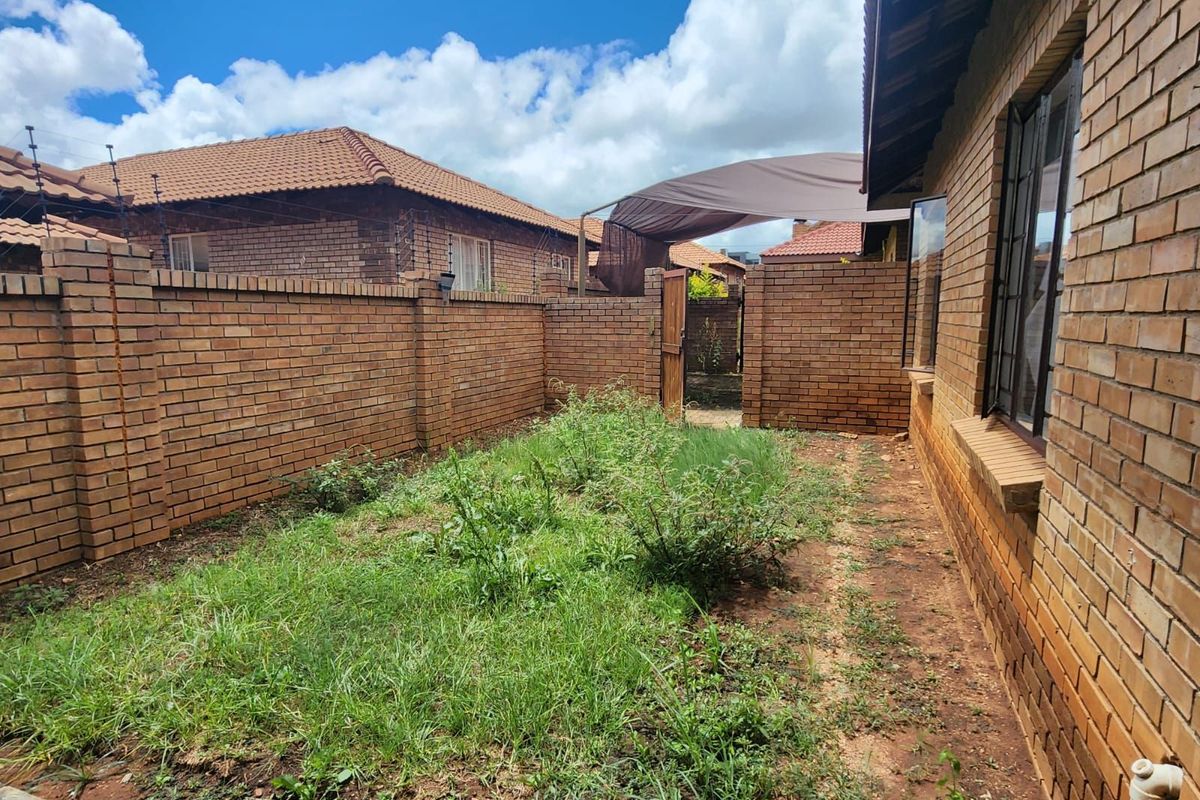 A rear garden area featuring face-brick boundary walls, a small gate, and an overgrown lawn requiring landscaping and maintenance.