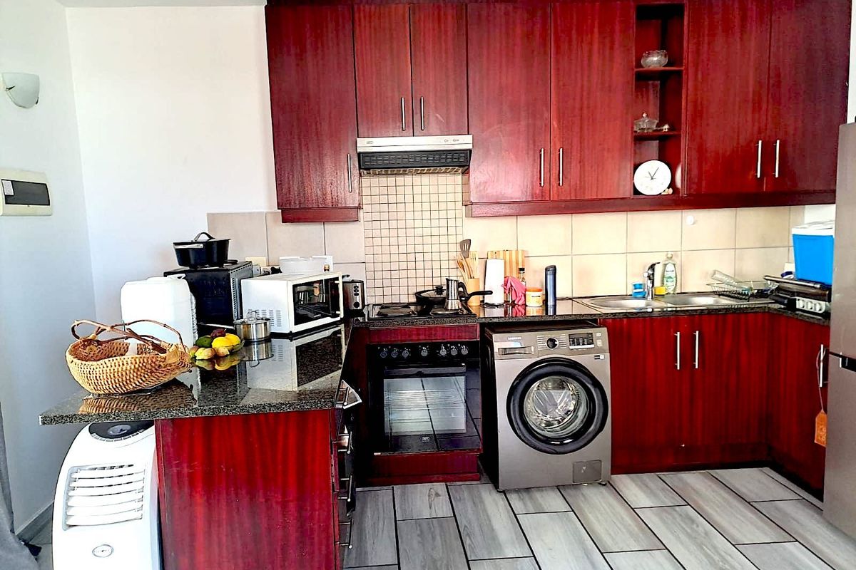 A functional kitchen featuring dark wood cabinetry, granite countertops, a built-in oven with hob, extractor fan, and an integrated washing machine.