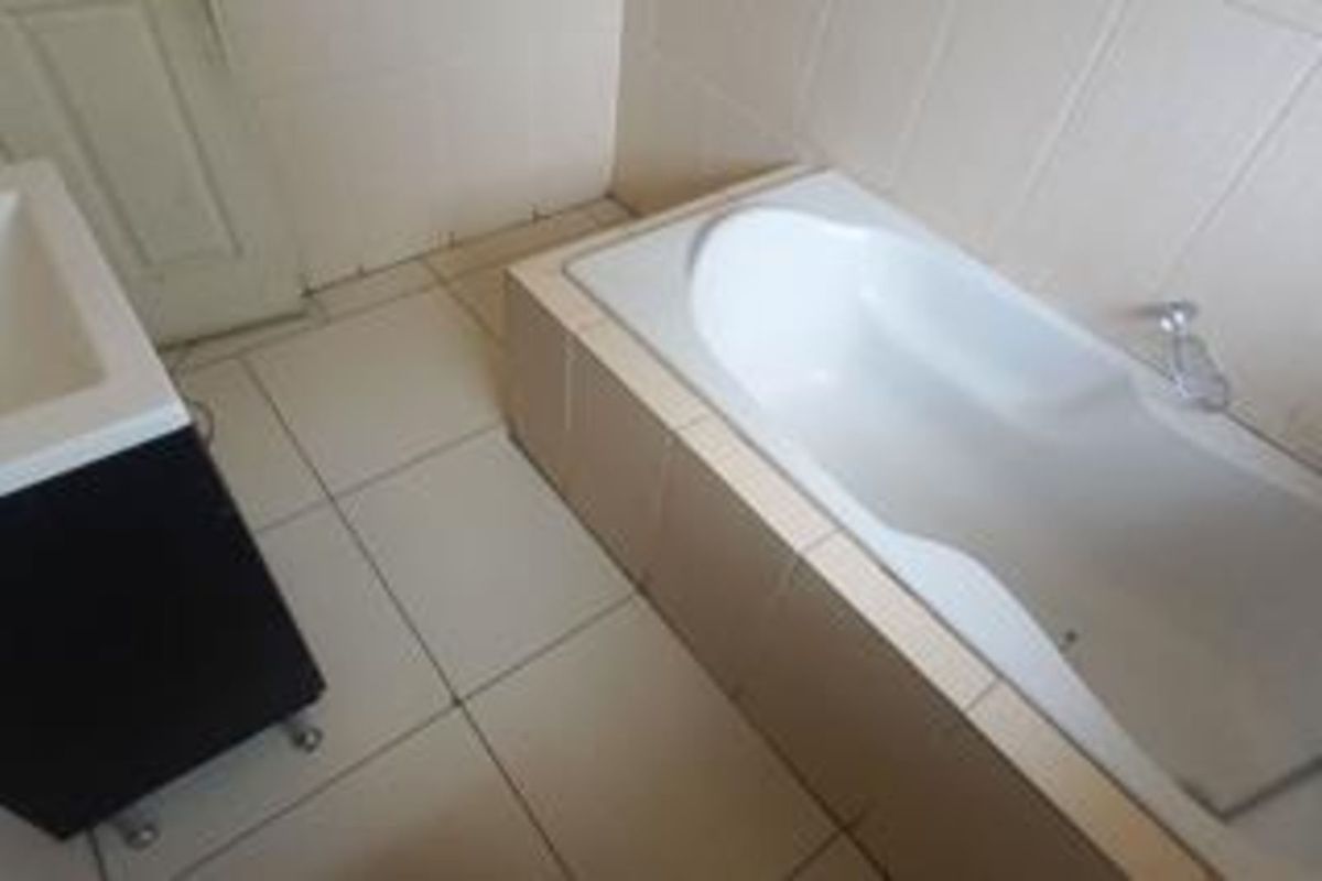 A functional bathroom featuring a built-in bathtub with tiled surround and a modern vanity unit.
