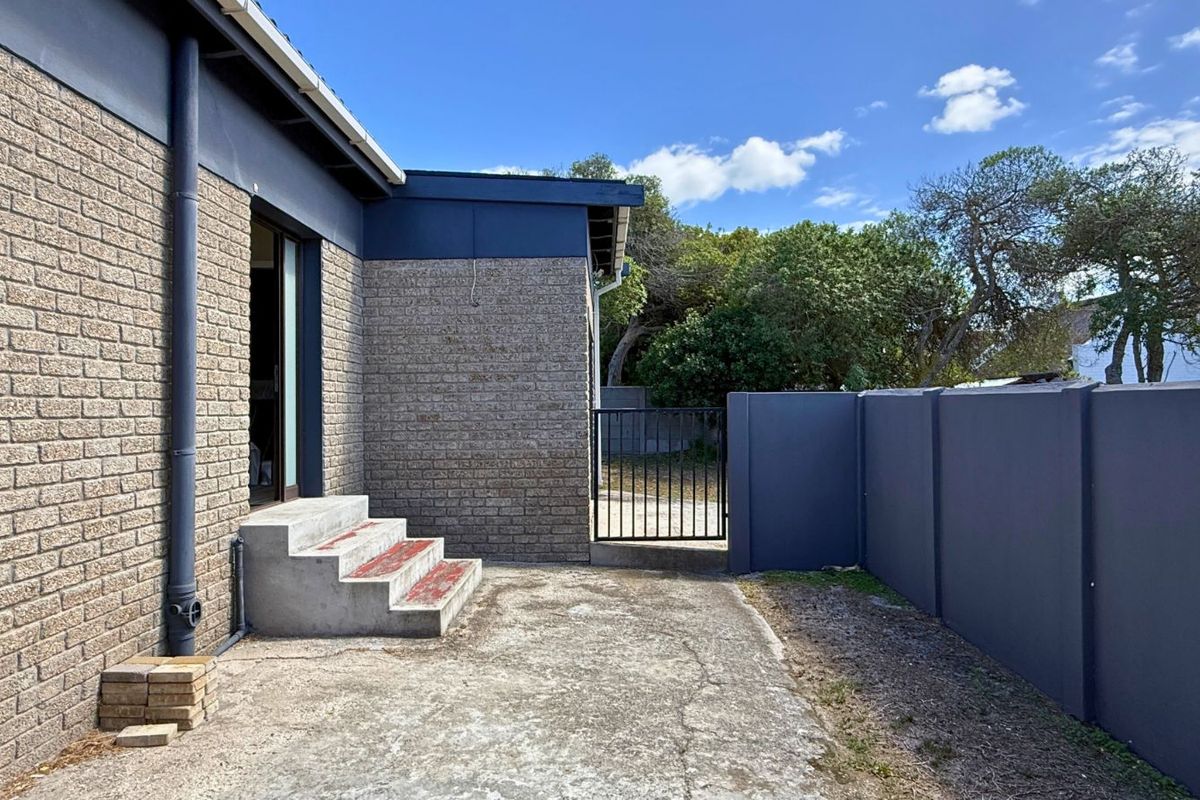 A rear exterior view featuring a brick facade, concrete patio area, and a secure metal gate leading to the garden.