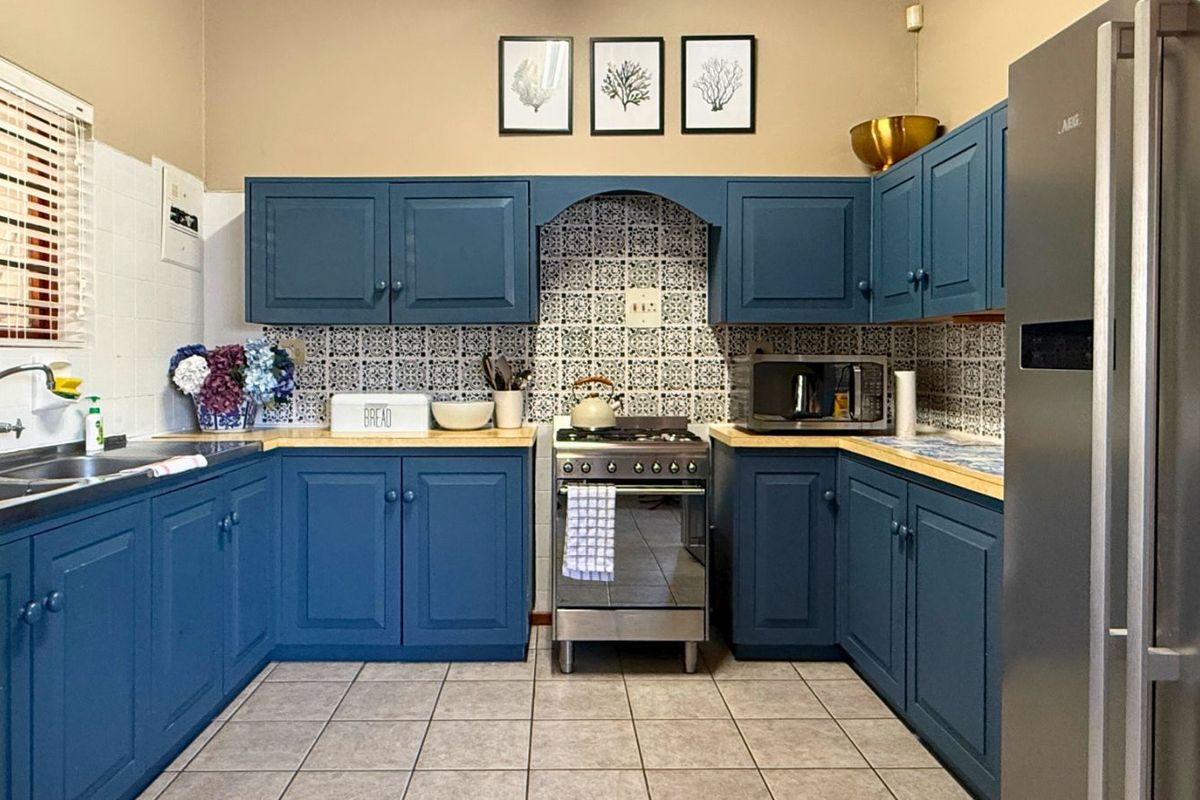 A functional kitchen featuring blue cabinetry, patterned tile backsplash, light-toned countertops, and a stainless steel gas stove.