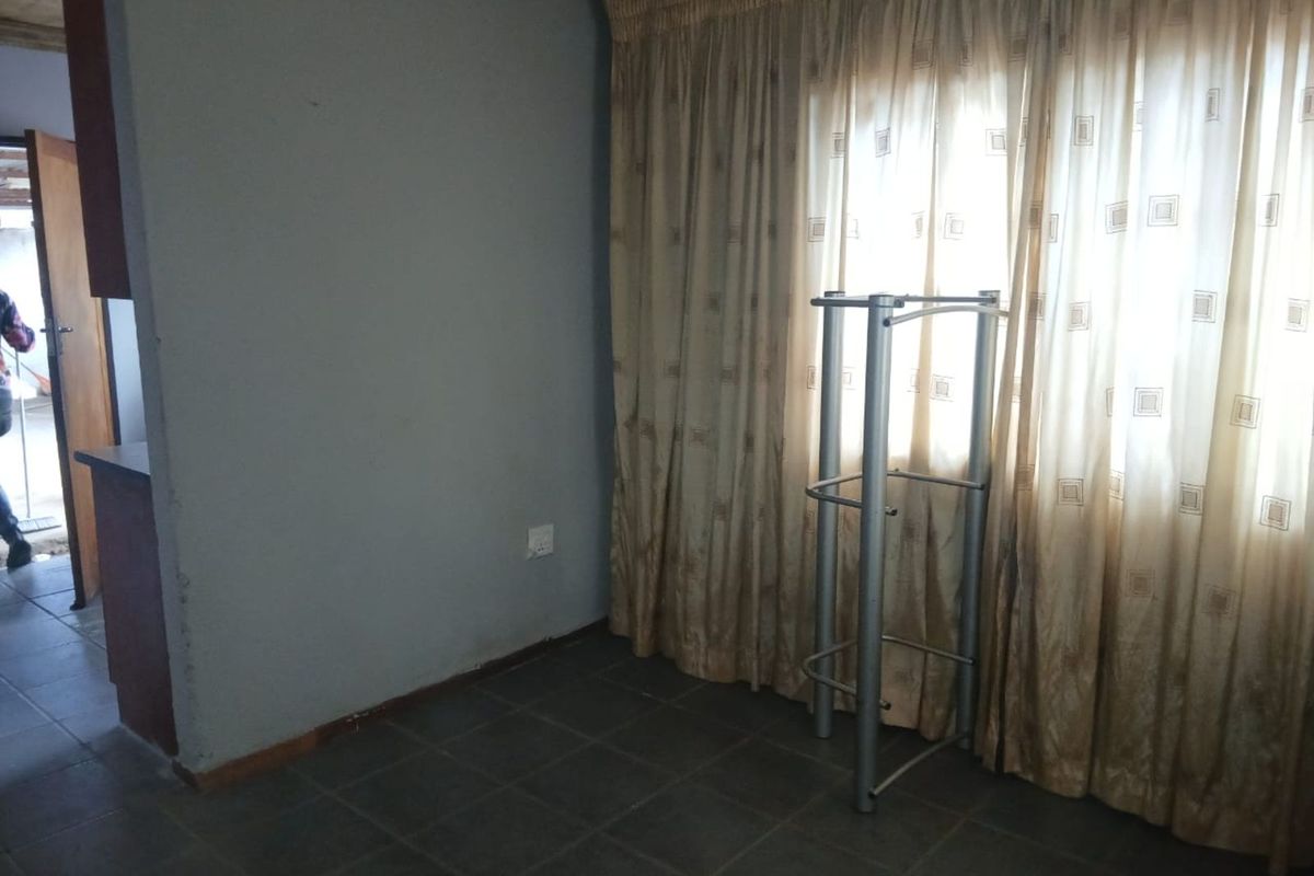 A living area featuring tiled flooring and large window curtains, providing a functional space with potential for cosmetic updates.