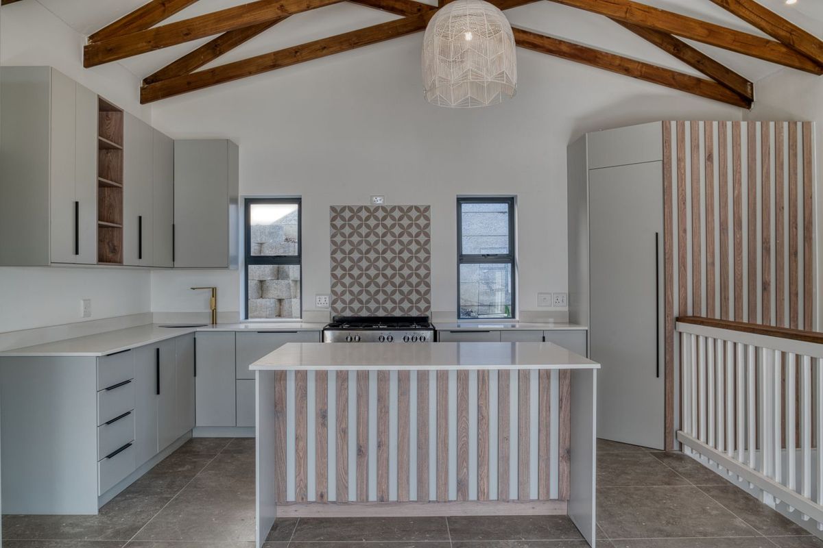 Modern kitchen featuring light grey cabinetry, a central island with wood-slat detailing, stone countertops, a gas stove, and exposed timber roof trusses.