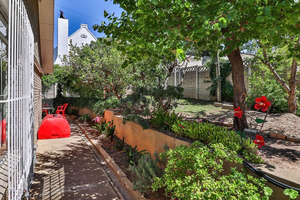A private rear garden featuring a concrete pathway, established trees, and a tiered retaining wall structure.
