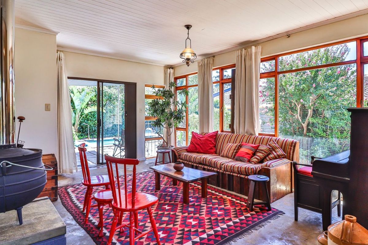 A bright living room featuring a cast iron fireplace, large windows with garden views, and sliding glass doors leading to the outdoor pool area.