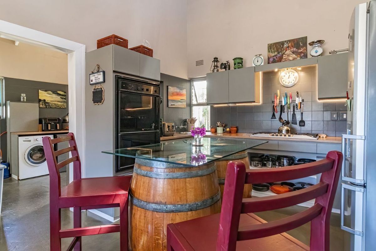 A functional kitchen featuring grey cabinetry, built-in oven, hob, and tiled splashback, with an adjacent laundry area visible through the doorway.