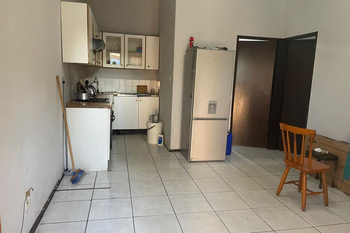 A compact kitchen area featuring white cabinetry, tiled flooring, and a functional layout, suitable for renovation to modernize the space.