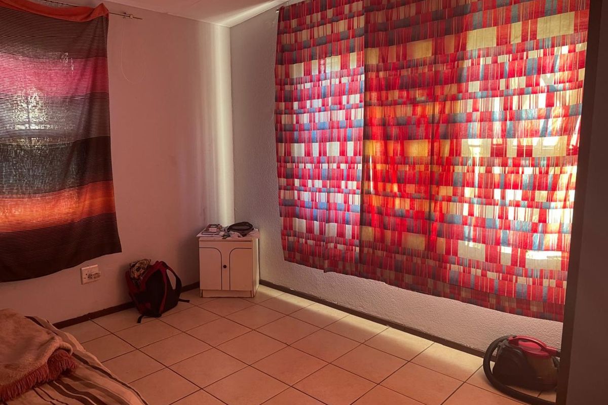 A bedroom featuring tiled flooring and large windows covered by decorative fabric panels, providing a functional living space.