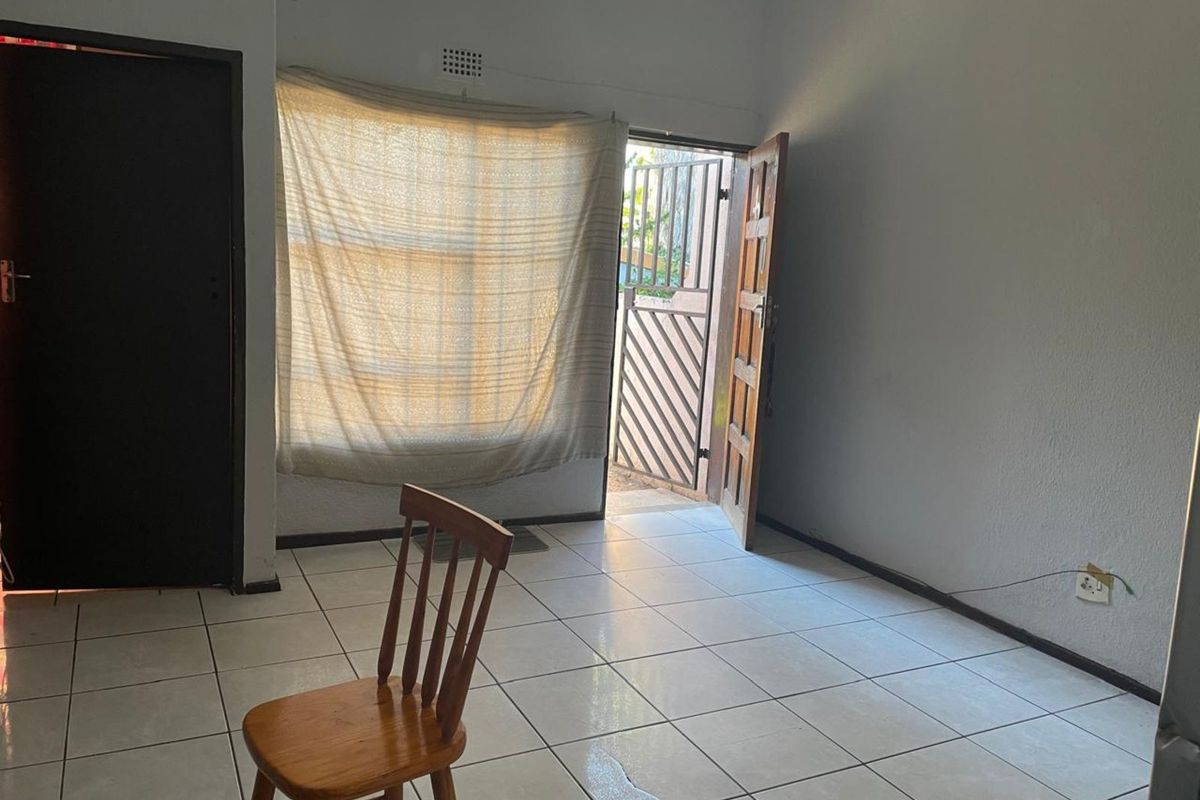 A simple living area featuring tiled flooring, a security gate at the entrance, and direct access to the exterior.