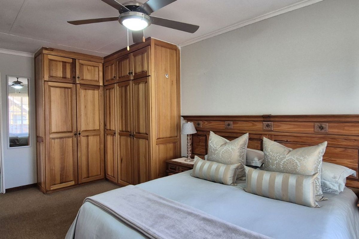A well-maintained bedroom featuring built-in wooden cabinetry, a matching wooden headboard, and an en-suite bathroom with modern vanity.