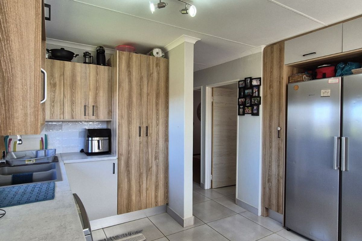 A functional kitchen featuring wood-grain cabinetry, tiled flooring, and integrated storage space, leading into a hallway.