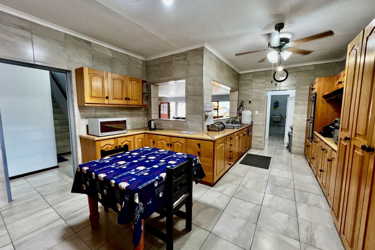 Spacious kitchen featuring extensive wooden cabinetry, tiled walls and flooring, built-in oven, and a ceiling fan, offering a functional layout with ample storage.