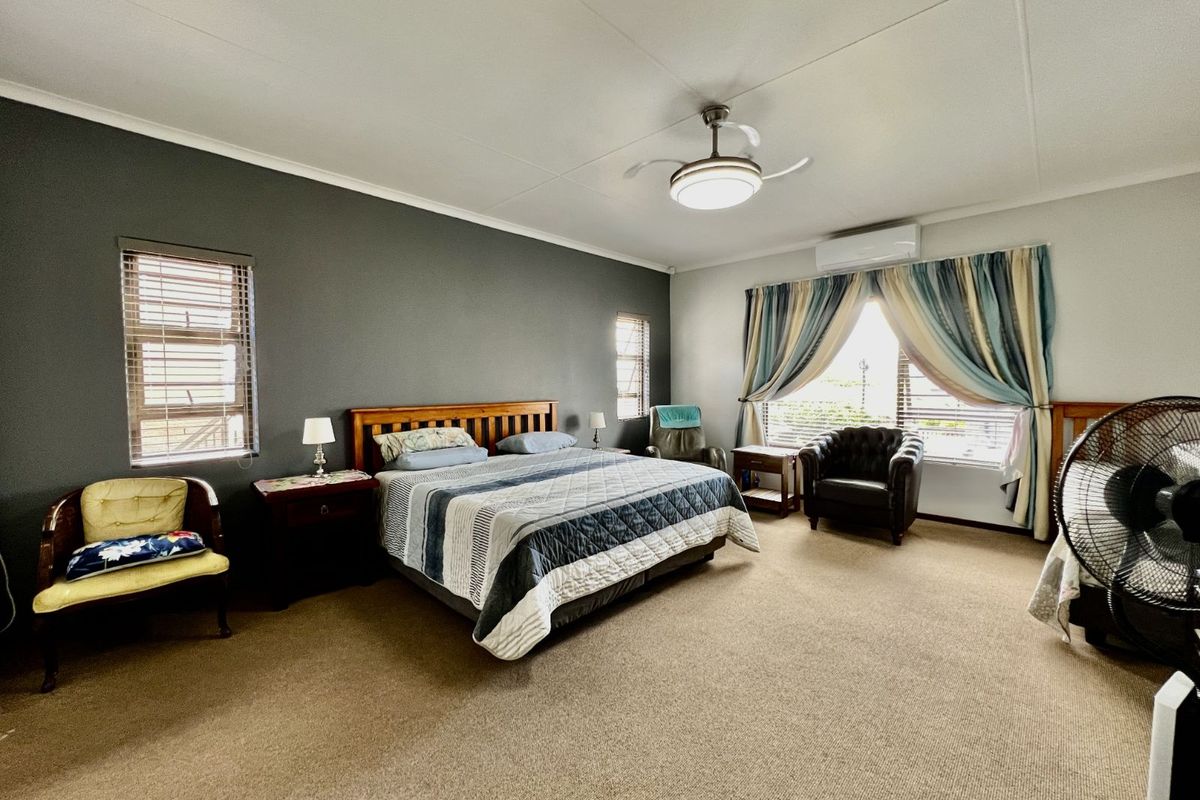 Spacious bedroom featuring a neutral carpet, a dark accent wall, a ceiling fan, and a wall-mounted air conditioning unit.