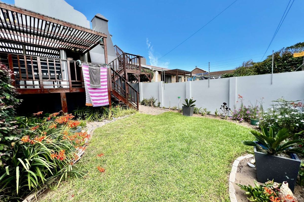 A private rear garden featuring a raised timber deck with pergola, external staircase, and a well-maintained lawn enclosed by high boundary walls.