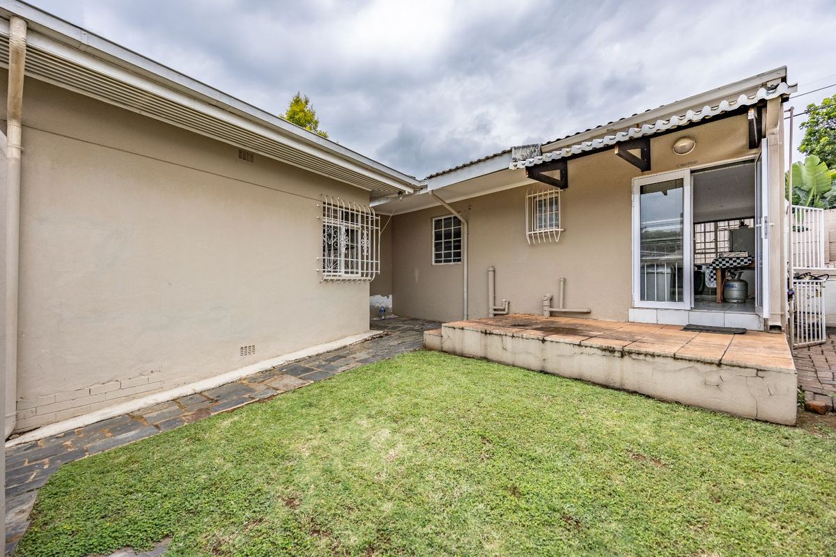 Rear exterior view of the property featuring a small lawn, paved walkway, and a raised patio area accessible through a glass door.