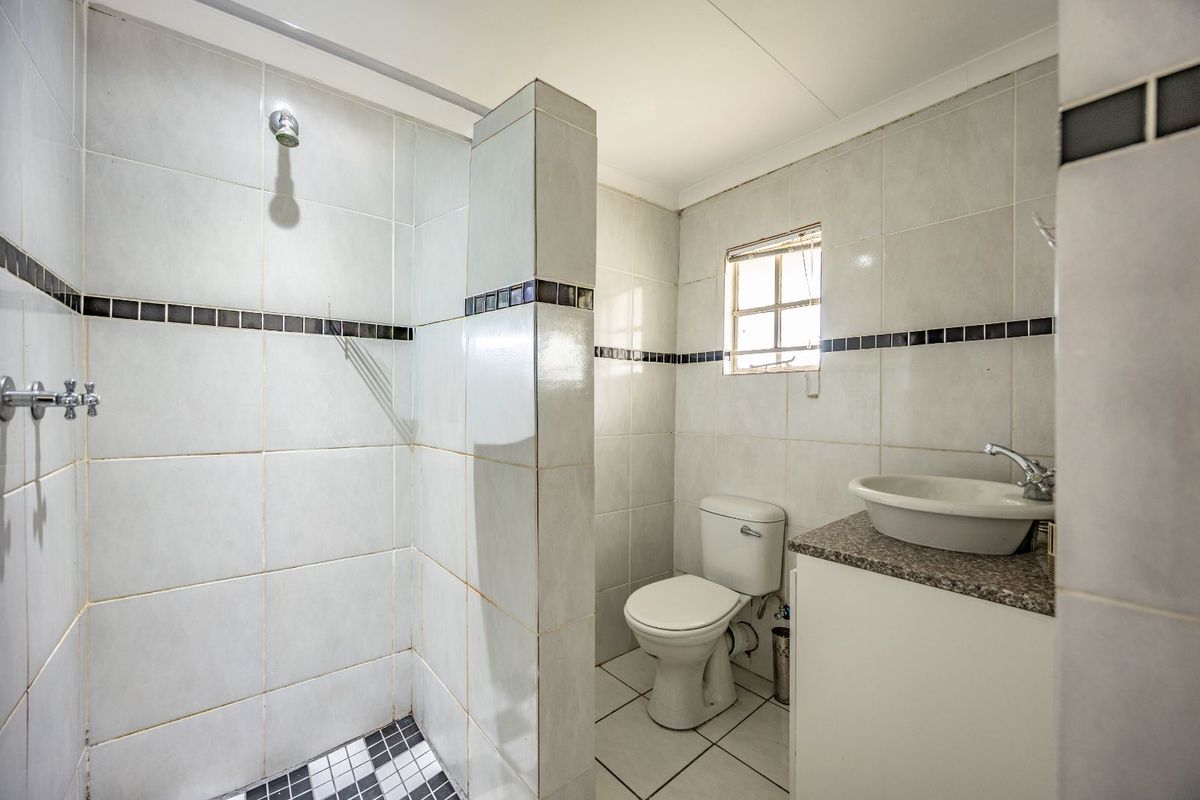 A functional bathroom featuring a walk-in shower, a pedestal-style vanity with a stone countertop, and a standard toilet with tiled walls and flooring.