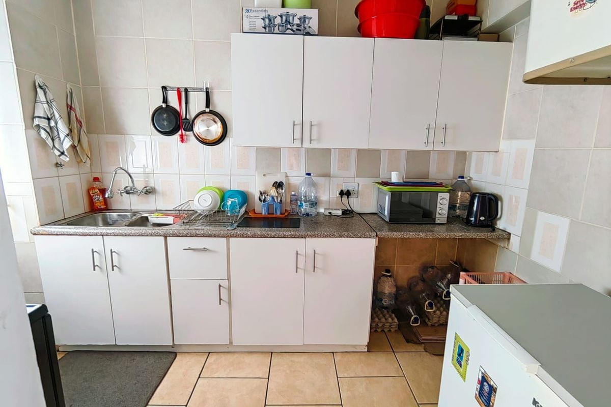 A functional kitchen featuring white cabinetry, granite-look countertops, tiled splashbacks, and a stainless steel sink with a mixer tap.