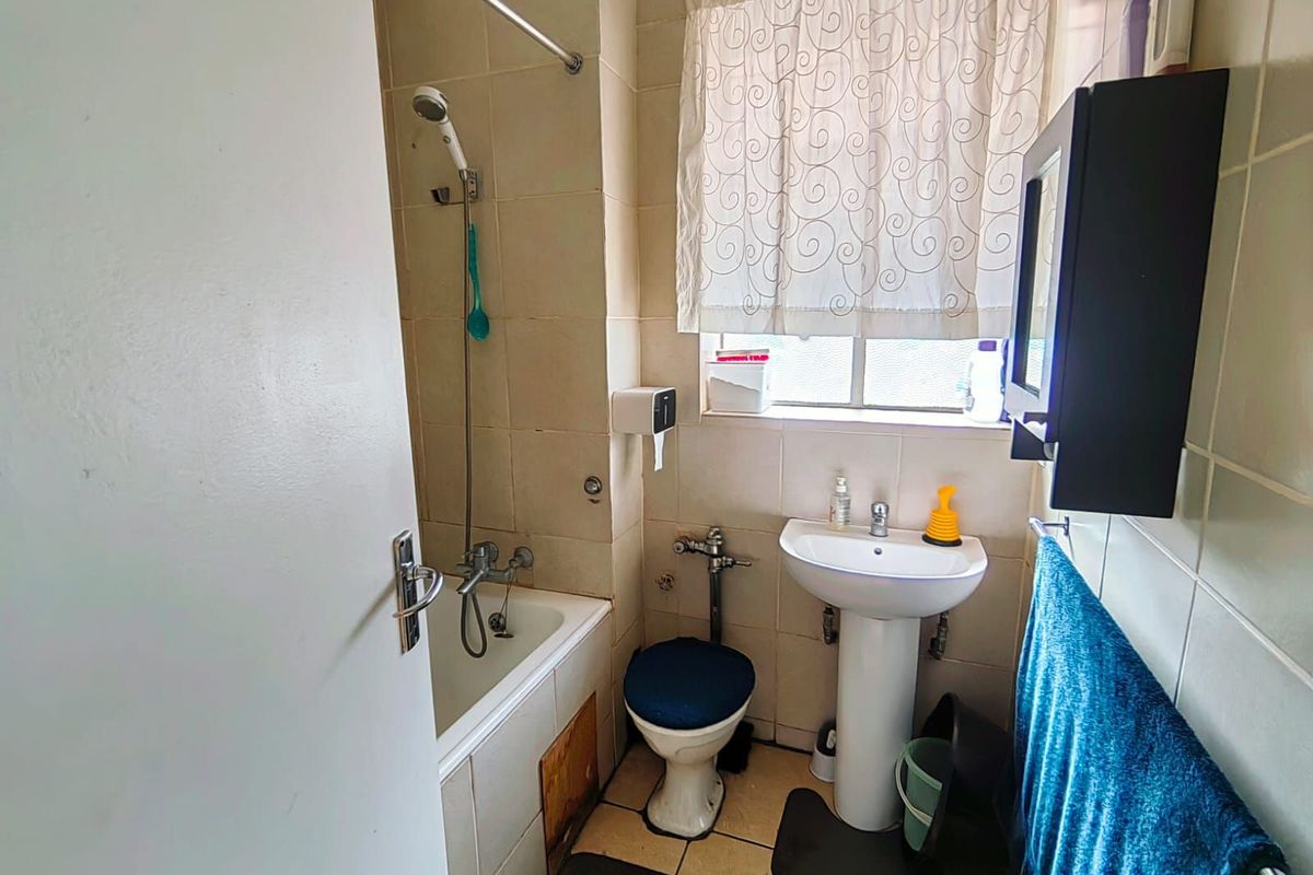 A compact bathroom featuring a pedestal basin, a bathtub with a shower attachment, and tiled walls, requiring some cosmetic updates.