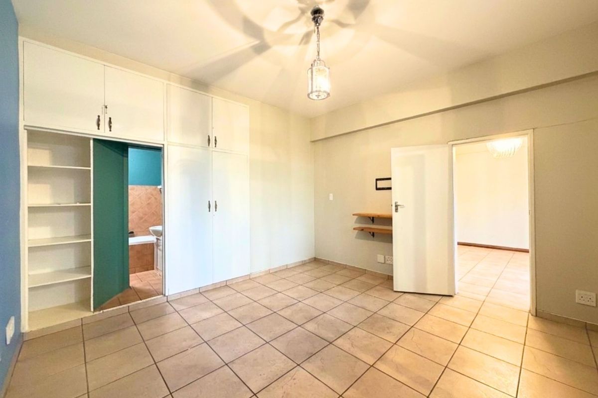 A spacious bedroom featuring built-in cupboards, tiled flooring, and direct access to an en-suite bathroom.